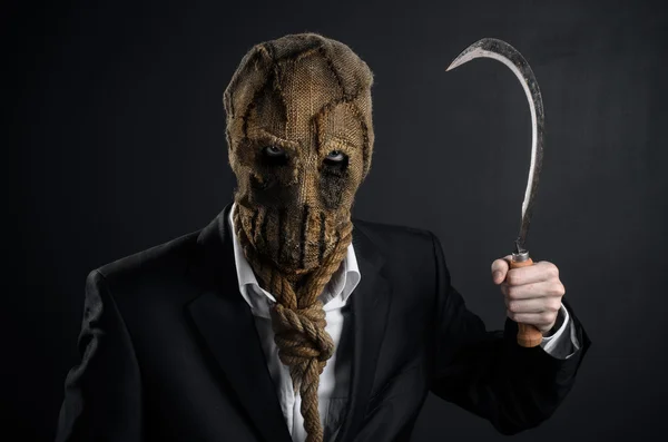 Fear and Halloween theme: a brutal killer in a mask holding a sickle old on a dark background in the studio — Stok fotoğraf