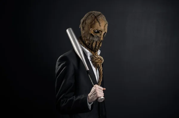 Fear and Halloween theme: a brutal killer in a mask holding a bat on a dark background in the studio — 图库照片