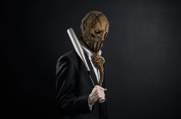 Fear and Halloween theme: a brutal killer in a mask holding a bat on a dark background in the studio — Stok fotoğraf