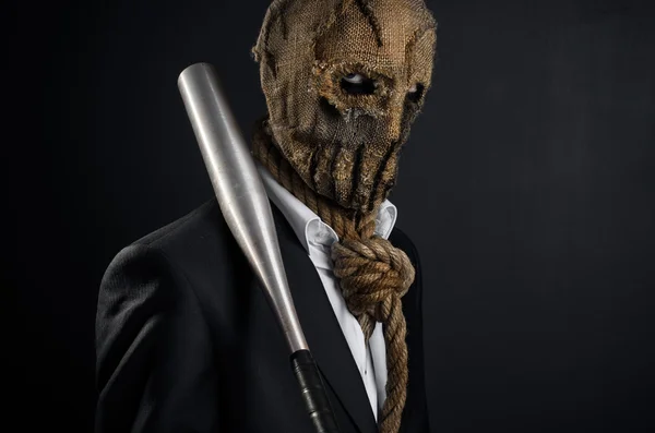 Fear and Halloween theme: a brutal killer in a mask holding a bat on a dark background in the studio — Stok fotoğraf