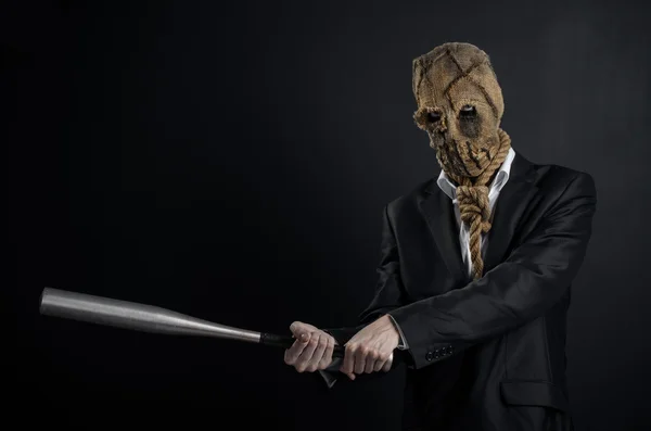 Fear and Halloween theme: a brutal killer in a mask holding a bat on a dark background in the studio — Stok fotoğraf