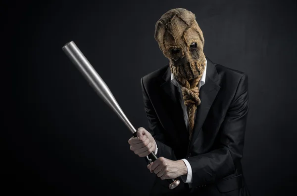 Paura e tema di Halloween: un brutale assassino in maschera che tiene un pipistrello su uno sfondo scuro in studio — Foto Stock