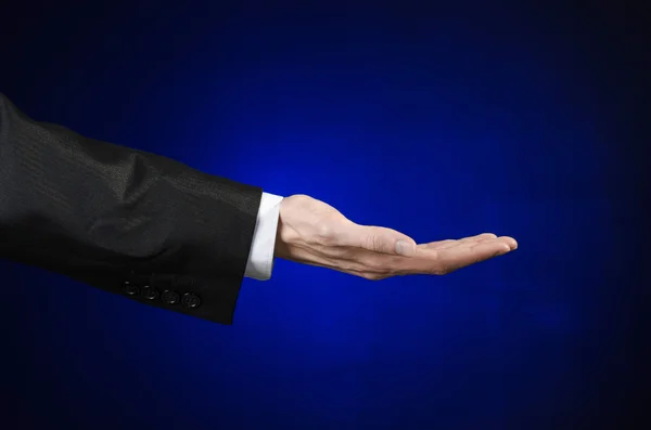 Бізнесмен і тема жесту: чоловік у чорному костюмі та білій сорочці, що показує жест рук на ізольованому темно-синьому фоні в студії — стокове фото