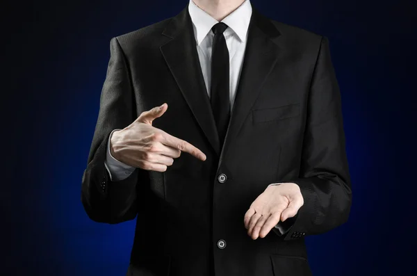 Businessman and gesture topic: a man in a black suit and white shirt showing gestures with hands on a dark blue background in studio isolated — Stock Photo, Image