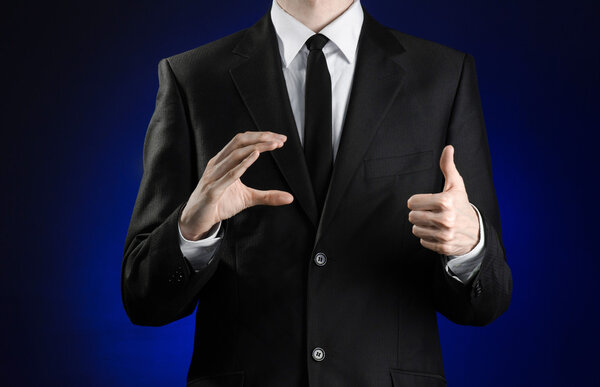 Предприниматель и тема жеста: человек в черном костюме и белой рубашке, показывающий жесты с руками на темно-синем фоне в изолированной студии
