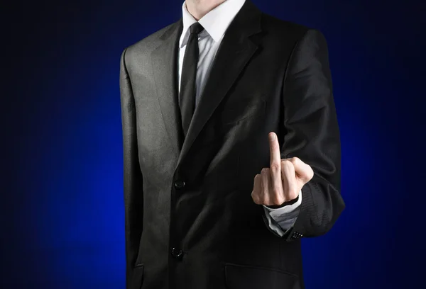 Businessman and gesture topic: a man in a black suit and white shirt showing middle finger gesture on a dark blue background in studio isolated — Stok fotoğraf
