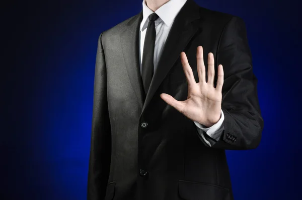 Businessman and gesture topic: a man in a black suit and white shirt showing gestures with hands palm against the dark blue isolated background in studio — Stock Photo, Image