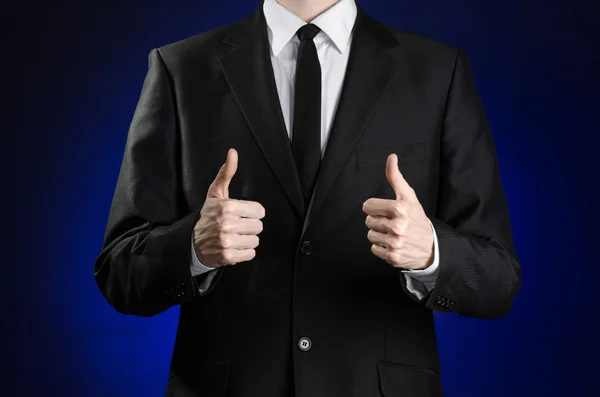 Businessman and gesture topic: a man in a black suit and white shirt showing hand gestures a thumbs-up on a dark blue background in studio isolated — Zdjęcie stockowe