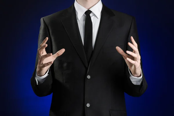 Businessman and gesture topic: a man in a black suit and white shirt showing gestures with hands on a dark blue background in studio isolated — Stock fotografie