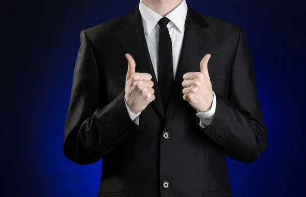 Businessman and gesture topic: a man in a black suit and white shirt showing hand gestures a thumbs-up on a dark blue background in studio isolated — Stok fotoğraf