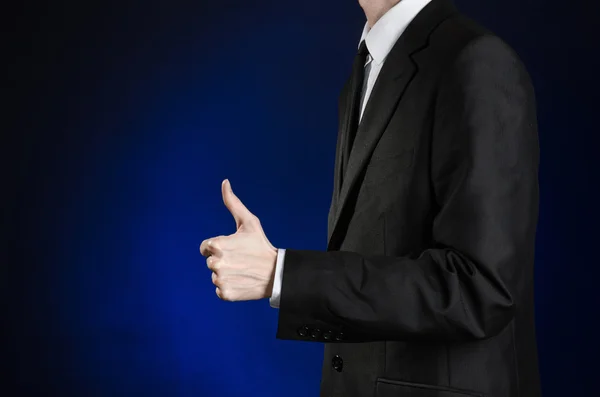 Businessman and gesture topic: a man in a black suit and white shirt showing hand gestures a thumbs-up on a dark blue background in studio isolated — Stok fotoğraf