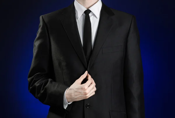 Предприниматель и тема жеста: человек в черном костюме и белой рубашке, исправляющий куртку и галстук на темно-синем фоне в изолированной студии — стоковое фото