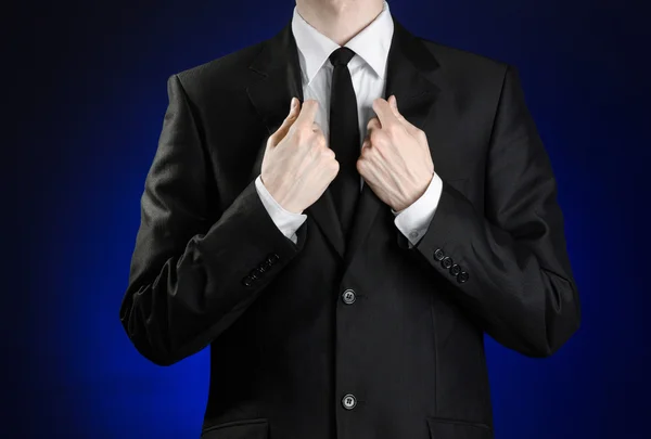 Businessman and gesture topic: a man in a black suit and white shirt correcting a jacket and tie on a dark blue background in studio isolated — 图库照片