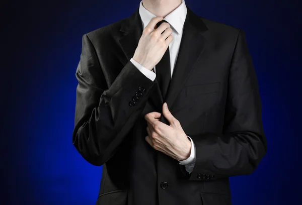 Businessman and gesture topic: a man in a black suit and white shirt correcting a jacket and tie on a dark blue background in studio isolated — Stock fotografie