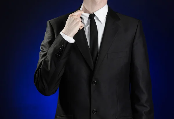 Businessman and gesture topic: a man in a black suit and white shirt correcting a jacket and tie on a dark blue background in studio isolated — Stockfoto