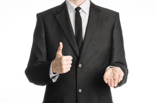 Businessman and gesture topic: a man in a black suit with a tie shows the right hand thumb up and holding his left hand on an isolated white background in studio — Stok fotoğraf