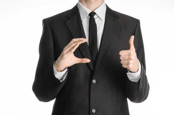 Uomo d'affari e tema del gesto: un uomo in abito nero e cravatta tiene la mano destra e la sinistra mostra un segno pollice-up isolato su sfondo bianco in studio — Foto Stock