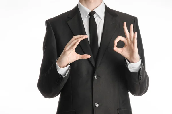 Hombre de negocios y tema de gesto: un hombre con un traje negro y corbata sostiene su mano derecha y la izquierda muestra un signo de bien aislado sobre fondo blanco en el estudio — Foto de Stock
