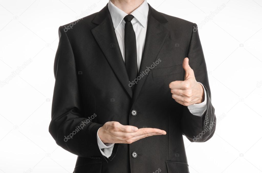 Businessman and gesture topic: a man in a black suit and tie with his left hand shows a thumbs up sign and holding his right hand on a white isolated background in studio