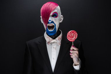 Clown and Halloween theme: Scary clown with pink hair in a black jacket with candy in hand on a dark background in the studio