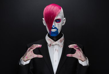 Clown and Halloween theme: Scary clown with pink hair in a black jacket on a dark background in the studio