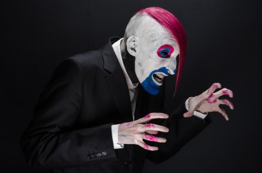 Clown and Halloween theme: Scary clown with pink hair in a black jacket on a dark background in the studio