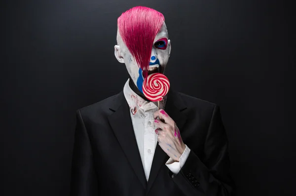 Clown and Halloween theme: Scary clown with pink hair in a black jacket with candy in hand on a dark background in the studio — Φωτογραφία Αρχείου