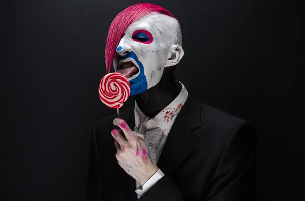 Clown and Halloween theme: Scary clown with pink hair in a black jacket with candy in hand on a dark background in the studio — Φωτογραφία Αρχείου