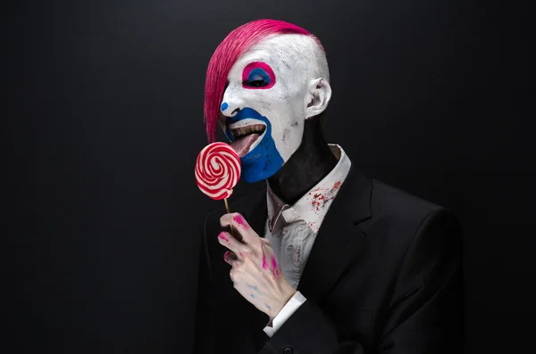 Clown and Halloween theme: Scary clown with pink hair in a black jacket with candy in hand on a dark background in the studio — Φωτογραφία Αρχείου