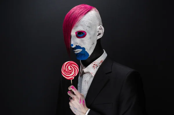 Palhaço e tema de Halloween: Palhaço assustador com cabelo rosa em uma jaqueta preta com doces na mão em um fundo escuro no estúdio — Fotografia de Stock