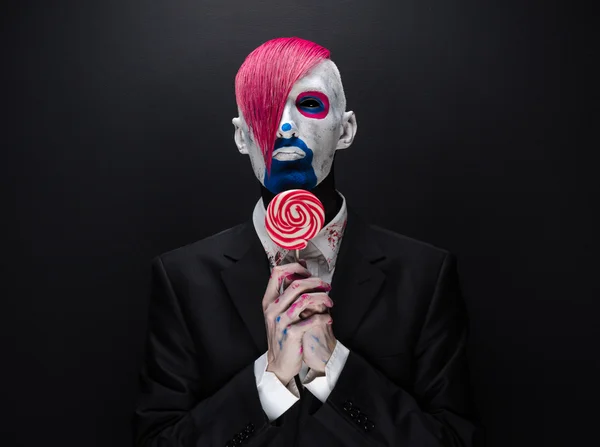 Clown and Halloween theme: Scary clown with pink hair in a black jacket with candy in hand on a dark background in the studio — 图库照片