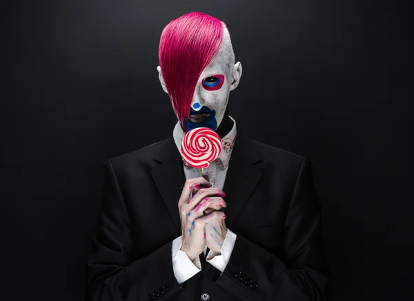 Clown et Halloween thème : Clown effrayant avec les cheveux roses dans une veste noire avec des bonbons à la main sur un fond sombre dans le studio — Photo