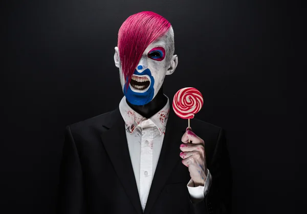 Clown and Halloween theme: Scary clown with pink hair in a black jacket with candy in hand on a dark background in the studio — 图库照片