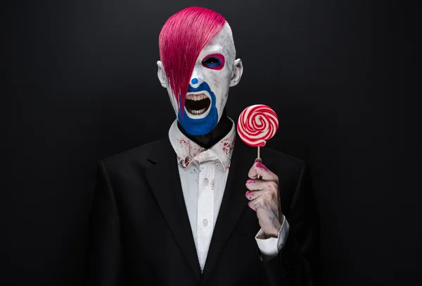 Clown and Halloween theme: Scary clown with pink hair in a black jacket with candy in hand on a dark background in the studio — 图库照片