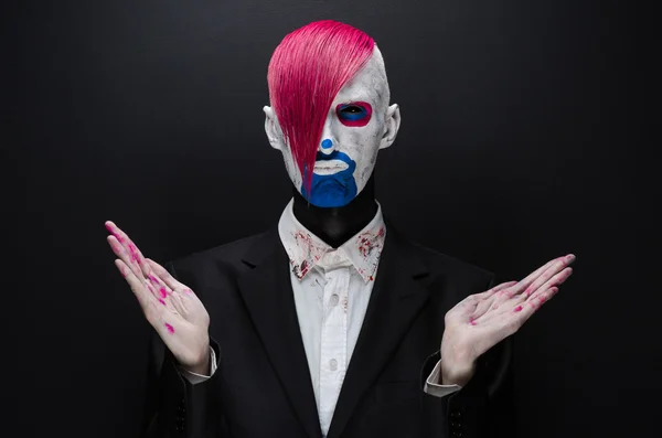 Clown and Halloween theme: Scary clown with pink hair in a black jacket on a dark background in the studio