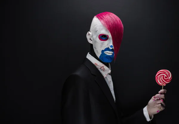 Clown and Halloween theme: Scary clown with pink hair in a black jacket with candy in hand on a dark background in the studio — Stock fotografie