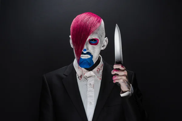 Clown et Halloween thème : Clown effrayant avec les cheveux roses dans un costume noir avec un couteau à la main sur un fond sombre dans le studio — Photo