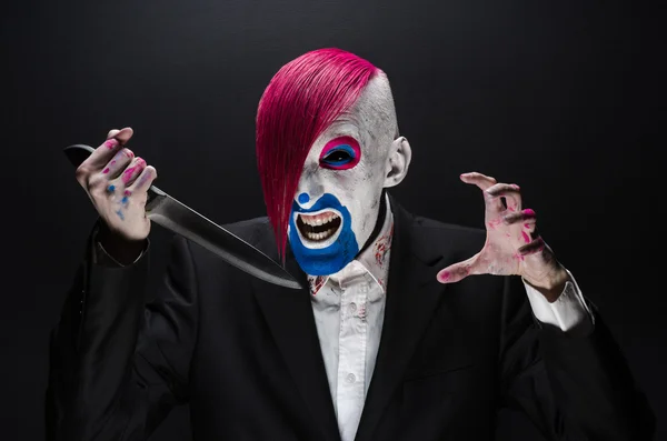Clown and Halloween theme: Scary clown with pink hair in a black suit with a knife in his hand on a dark background in the studio — 图库照片