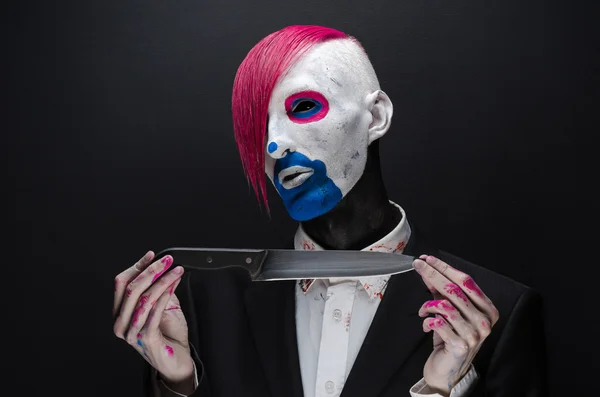 Clown and Halloween theme: Scary clown with pink hair in a black suit with a knife in his hand on a dark background in the studio — 图库照片