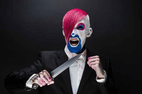 Clown and Halloween theme: Scary clown with pink hair in a black suit with a knife in his hand on a dark background in the studio — Stockfoto