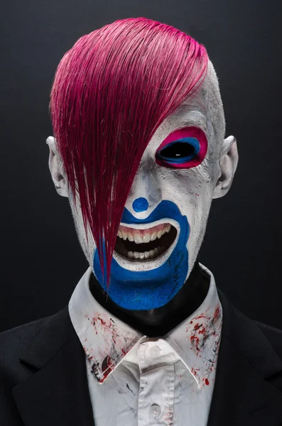 Clown and Halloween theme: Scary clown with pink hair in a black jacket on a dark background in the studio