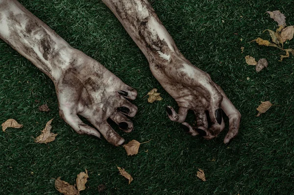 Horror en Halloween thema: verschrikkelijke zombie handen vuil met zwarte nagels liggen op het groene gras, de walking dead Apocalyps, top weergave — Stockfoto