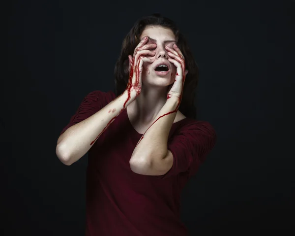 Страшная девушка и тема Хэллоуина: портрет сумасшедшей девушки с окровавленной рукой закрывает лицо в студии на темном фоне, кровавые слезы — стоковое фото