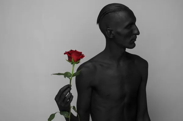 Gothic en Halloween thema: een man met zwarte huid houden een rode roos, zwarte dood geïsoleerd op een grijze achtergrond in studio — Stockfoto