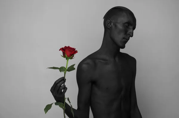 Θέμα της γοτθικού και Απόκριες: ένας άνθρωπος με μαύρο δέρμα κρατώντας ένα κόκκινο τριαντάφυλλο, Μαύρος Θάνατος απομονωμένη σε ένα γκρίζο φόντο στο στούντιο — Φωτογραφία Αρχείου