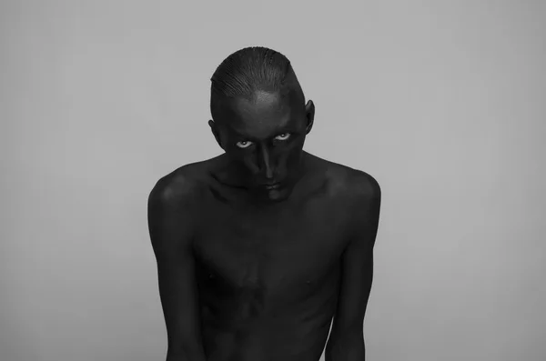 Gothic and Halloween theme: a man with black skin is isolated on a gray background in the studio, the Black Death body art — Stock Photo, Image