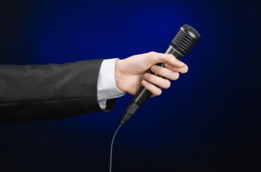 Business speech and topic: a man in a black suit holding a black microphone on a dark blue background in studio isolated