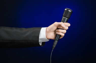 Business speech and topic: a man in a black suit holding a black microphone on a dark blue background in studio isolated