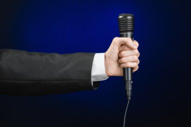 Business speech and topic: a man in a black suit holding a black microphone on a dark blue background in studio isolated