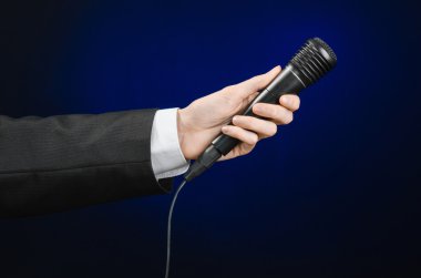 Business speech and topic: a man in a black suit holding a black microphone on a dark blue background in studio isolated